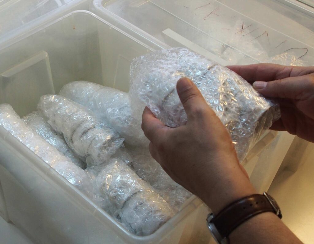 Hände verpacken einen Porzellanartikel, schon verpackte Teile liegen in einer Transportbox