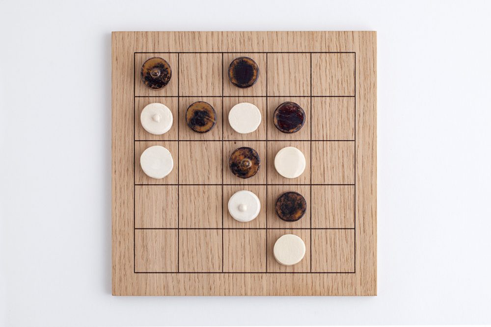 Brettspiel Gripps - ein hölzernes Spielbrett mit einem 5x5-Gitter und runden Spielsteinen in zwei Farben: hell (weiß) und dunkel (braun-schwarz marmoriert). Das Spielbrett liegt auf einem weißen Hintergrund.